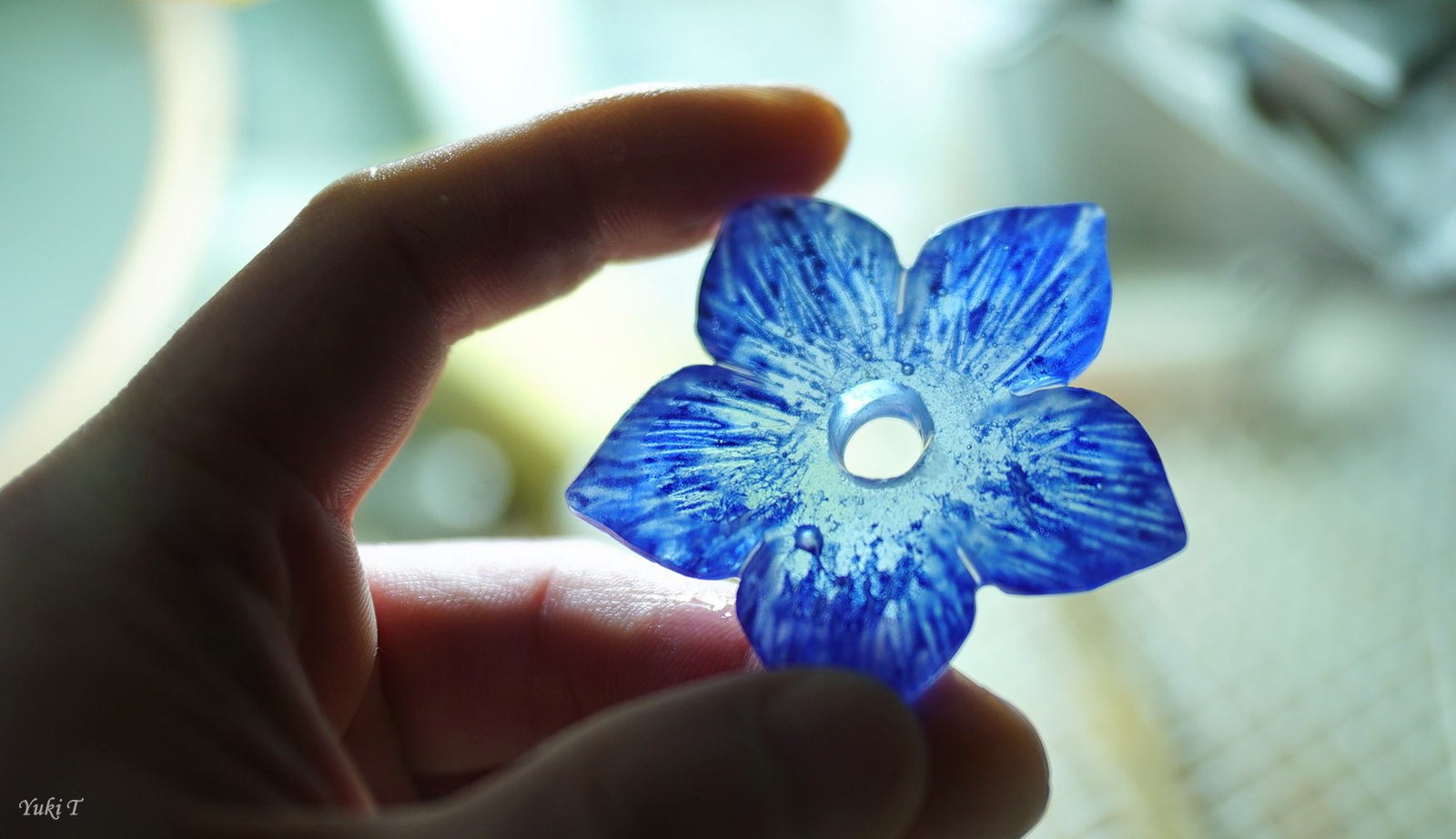 手に持ち光に透かした青い花形のガラス